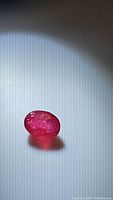 Photo of natural ruby showing oval cut and polished facets with visible inclusions under illumination.