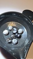 Eight round natural snowflake obsidian cabochons displayed in a black dish, showing distinctive black and gray-white snowflake inclusions.