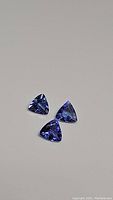 Three trillion cut tanzanite gemstones placed together showing blue and purple hues, photographed on a neutral background.