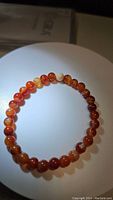 Photo of a natural red agate bead bracelet placed on a white circular platform showing the full circle of beads with varying reddish-orange hues and smooth polished finish.