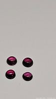 Four round cabochon pink-purple Rhodolite garnet stones displayed on a white background, showing color and smooth domed surfaces.