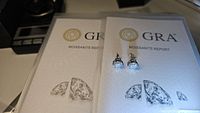 Pair of moissanite stud earrings atop two GRA Moissanite report booklets