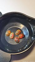 Five oval cabochon chocolate opals in black container showing varied bright rainbow flashes under light.