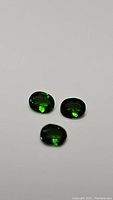 Three oval-shaped deep electric green Chrome Diopside gemstones arranged on a plain light background, showing color and clarity.