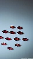 Thirteen marquis cut natural sapphires in fire red to pink hues laid out on white background, showing shape and color variations.