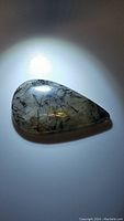 Pear-shaped black rutilated quartz cabochon with black tourmaline inclusions under bright light showing inclusions and clarity from one angle.
