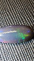 Close-up photo of oval cabochon Ethiopian black opal showing bright flash of green and blue colors on a black base.