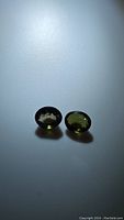 Two oval cut green tourmaline gemstones placed side by side, showing the color and cut under light.