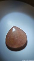 Photo of a large pear-shaped polished strawberry quartz cabochon with visible internal inclusions and a pink tint under bright light.