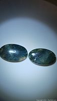 Pair of oval-shaped polished moss agate cabochon stones laid flat under focused lighting, showing translucent green colors with moss-like internal patterns.