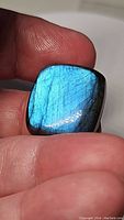 Close-up of the polished rectangular labradorite gemstone showing intense blue flash under light while held between fingers.