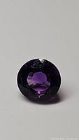 Close-up photo of deep purple round cut amethyst gemstone showing facets and color