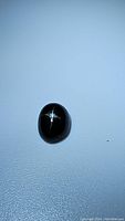 Oval cabochon black star diopside gemstone showing distinctive 4-ray star asterism.