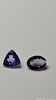 Pair of natural tanzanite loose gemstones on a grey background showing oval cut and trillion cut stones