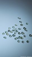 Scattered round cut alexandrite gemstones on white surface under neutral light