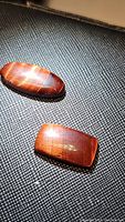 Pair of polished red tigerseye cabochons on black textured background showing their shape and hologram effect.