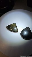 Photo of two natural obsidian polished gemstones, one gold sheen and one silver sheen, displayed on white surface under direct light revealing reflective sheen.