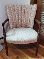 Front view of antique wooden armchair with scallop-shaped upholstered back and patterned fabric seat.