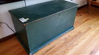 Front angle view of antique green painted wooden blanket chest showing surface wear and scratches.