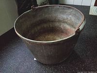 View showing the inside of the large weathered metal boiling pot with wrought iron rim and handle, revealing patina and wear from use.