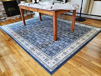View of the blue and off-white patterned area rug under a wooden dining table on hardwood flooring, showing overall design and condition.