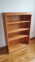Front view of the wooden bookcase showing four shelves and light brown wood finish.