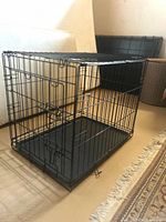 Front and side view of the black wire dog crate on a floor with a removable plastic tray inside.