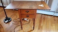 Vintage Sprague & Carlton maple wood 2-drawer drop leaf side table with the top leafs extended, showing stains and scuffs on the surface.