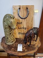 Photo showing entire lot on wooden table including leather horse figurine, ceramic horse sculpture, and horseshoe plaque