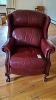Front view of the burgundy leather reclining wing back chair showing seat, armrests with nailhead trim, and ball and claw wooden feet.