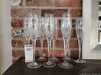 Set of 8 Mikasa crystal champagne flutes arranged on a surface against a brick wall, showing overall set and scale with MaxSold sticker for reference.