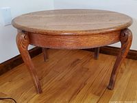 Front angle view of round oak wood coffee table showing carved cabriole legs and wood grain top.