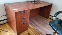 Front angle of the wooden office desk showing three drawers with black handles on the left side and clear top surface.