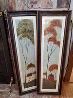 Pair of vertical framed art prints by Warren Kimble with wooden frames and pastoral scenes.