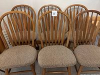 Front view of the six oak Windsor chairs with fabric cushions showing the seat and curved spindle backs.