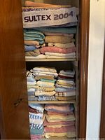 Closet shelf filled with neatly folded assorted bath towels and face towels in various colors and sizes.