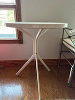 Side view of white metal round bistro table showing tripod leg design and smooth finish
