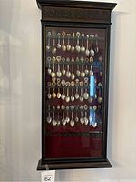 Front view of the closed hanging wooden spoon rack showing the display of many spoons inside behind glass door.