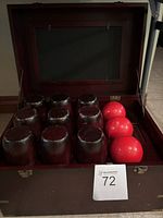 Interior of wooden box showing nine dark brown wooden bowling pins and three red wooden bowling balls arranged inside.