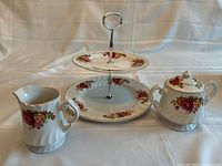 Full view of two-tiered dessert tray, creamer, and sugar bowl with lid showing floral pattern and metal handle on tray