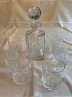 Full view of crystal decanter with stopper surrounded by six matching tumblers.