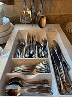 Image of the entire cutlery set arranged in the white divided ceramic tray with hanging utensils above
