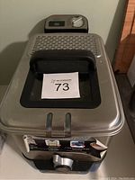 Top view of the deep fryer lid with black handle and auction lot number paper on top