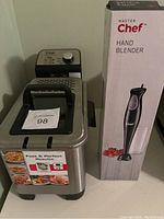 T-fal deep fryer and boxed Master Chef hand blender side by side on a white surface.