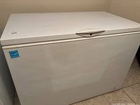 Closed view of the white chest freezer showing top and front sides with handle and lock.
