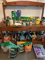 Overview of gardening supplies including soil bags, bottles of fertilizers and insect repellents, gloves, and watering can on wooden shelves