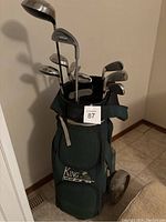 King Cobra green golf bag loaded with various golf clubs and visible pull cart wheels.