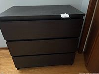 Front view of the black dresser showing three drawers with a label on top right corner.