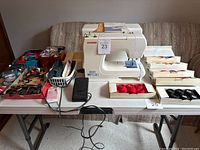 Overall view of the sewing machine with foot pedal, thread boxes, and containers of accessories on a table.