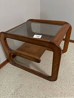 Angled side view of oak cantilevered two-tier side table showing cantilevered rectangular frame, glass top, and wooden lower shelf.
